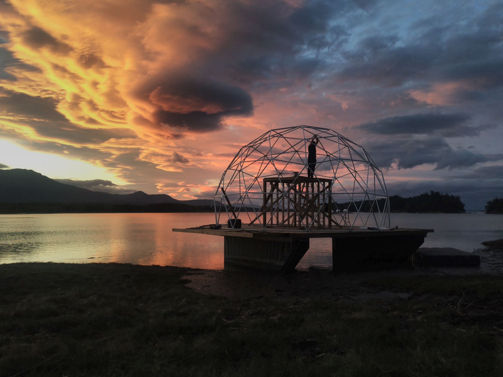 Prototype platform silhouetted on calm water beneath an orange dusk sky